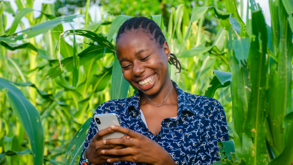 A farmer holding a smartphone showing an agricultural app in a green field
